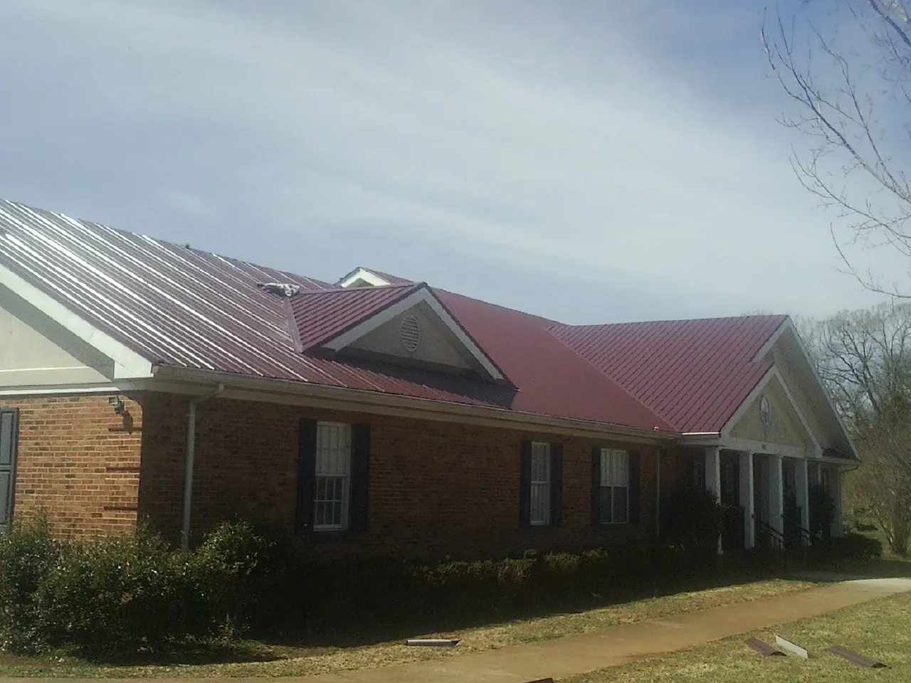 Red metal roof with gabled entries on a long brick building, from a Hail Damage Roof Repair job in Duryea