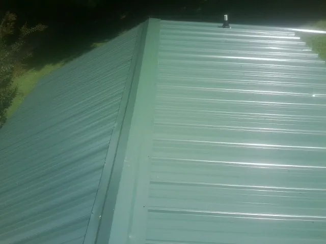 New green metal panels meeting at the ridge of a roof — Flat Roof Repair work by our crew in Duryea
