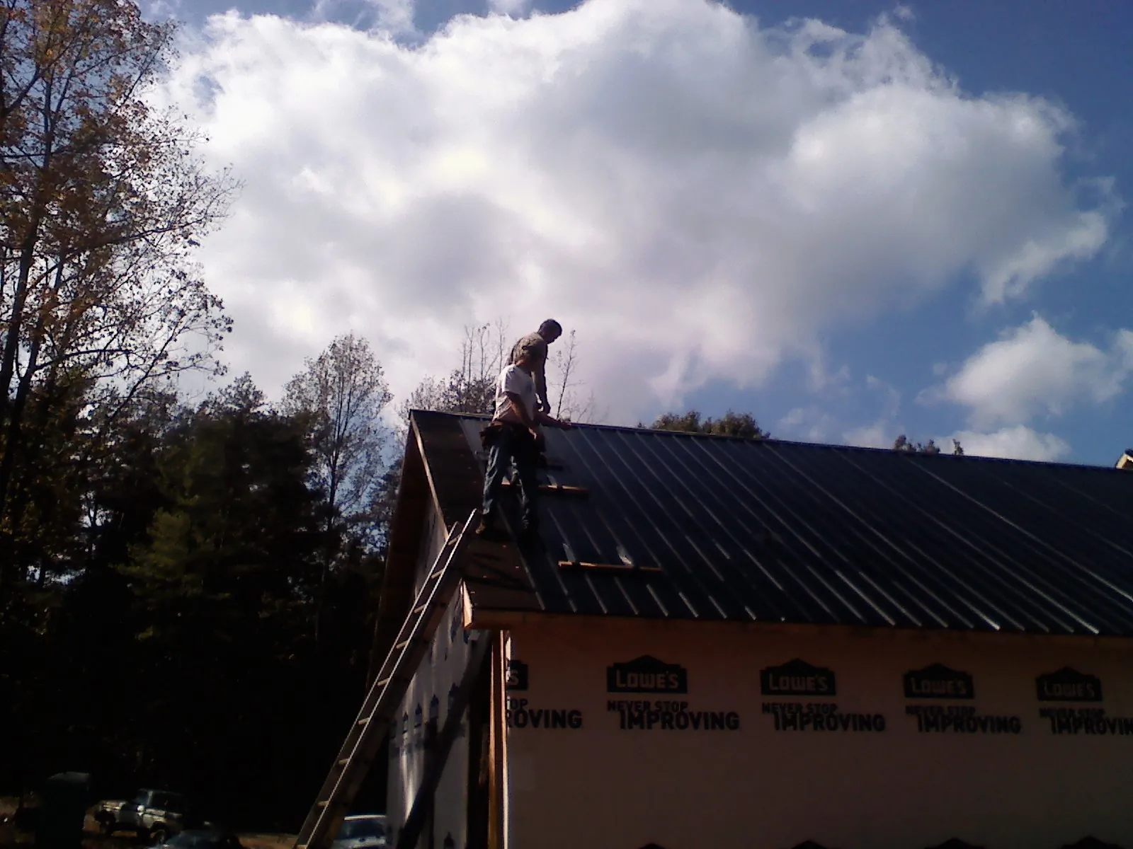 Roofer fastening dark metal panels high against a cloudy sky, from a Roof Inspection job in Duryea